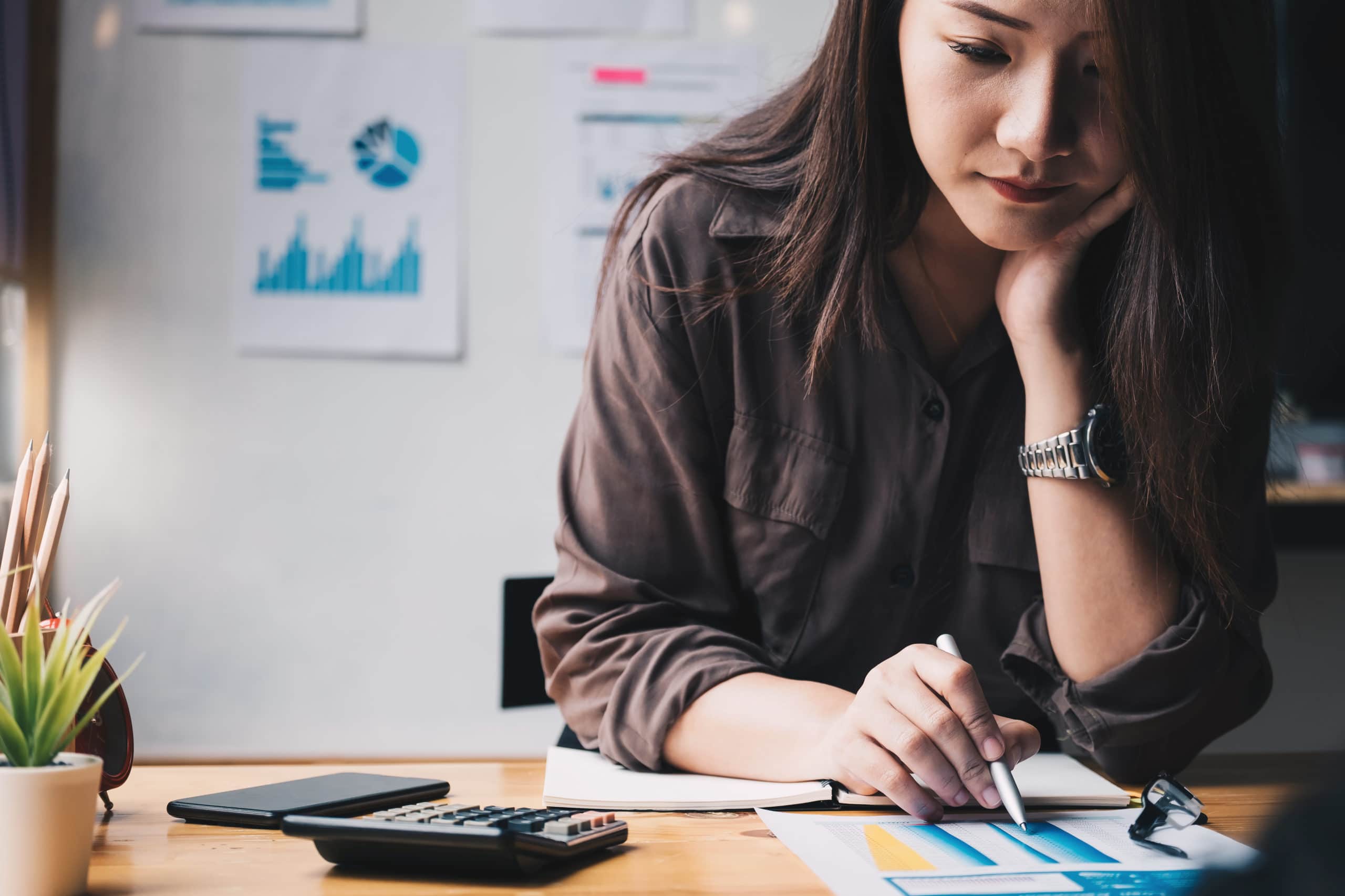 Young woman reviewing personal finance with spreadsheets and a calculator.