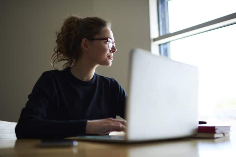 Young woman, recent graduate, working on a laptop, gazing, laptop