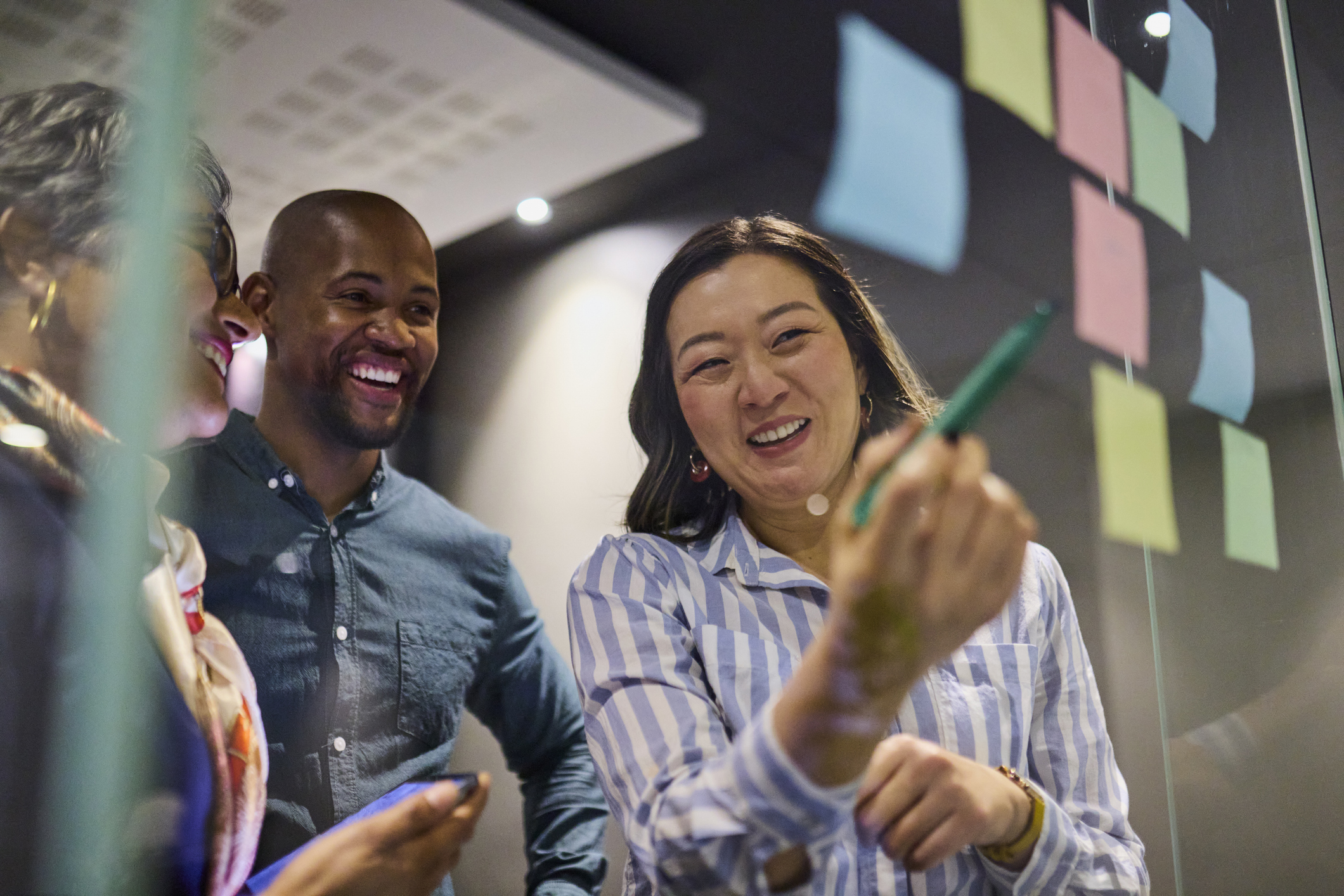 Diverse group collaborating on a glass wall covered with colorful sticky notes.